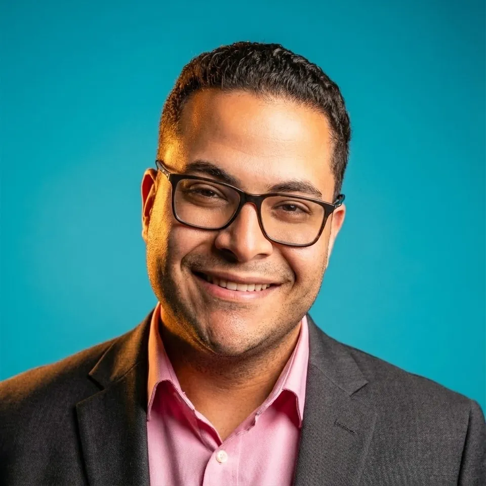 Fady Boules, PMHNP-BC, smiling in glasses, a charcoal blazer, and a rose-pink shirt.